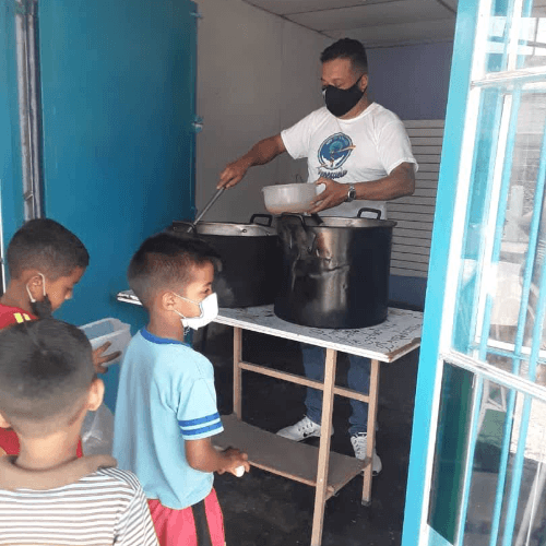 Volunteer serving food to kids lined up